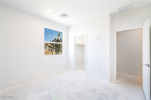 unfurnished bedroom featuring a walk in closet, unfinished concrete flooring, baseboards, and visible vents