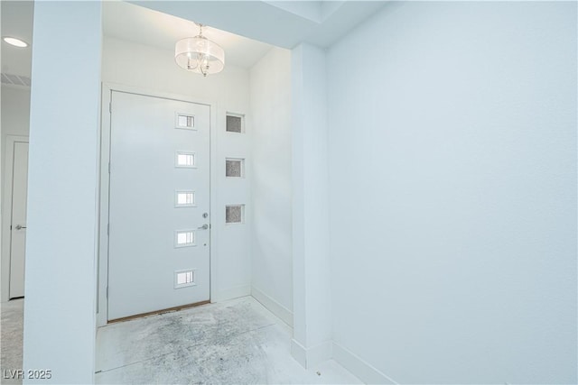 foyer entrance with baseboards, a notable chandelier, and concrete floors