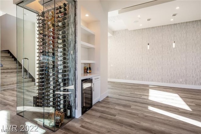 wine room with built in features, wine cooler, wood finished floors, and wallpapered walls