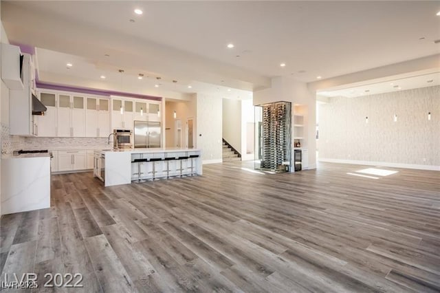 kitchen with wood finished floors, open floor plan, appliances with stainless steel finishes, exhaust hood, and a large island with sink