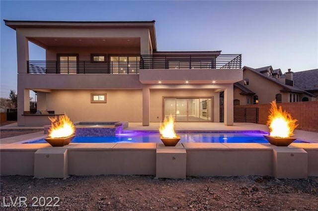 back of house with stucco siding, a fire pit, and a balcony