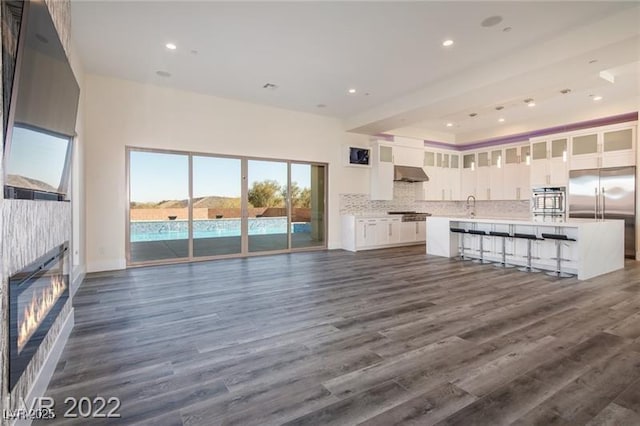 unfurnished living room with a glass covered fireplace, recessed lighting, a sink, and dark wood-style flooring