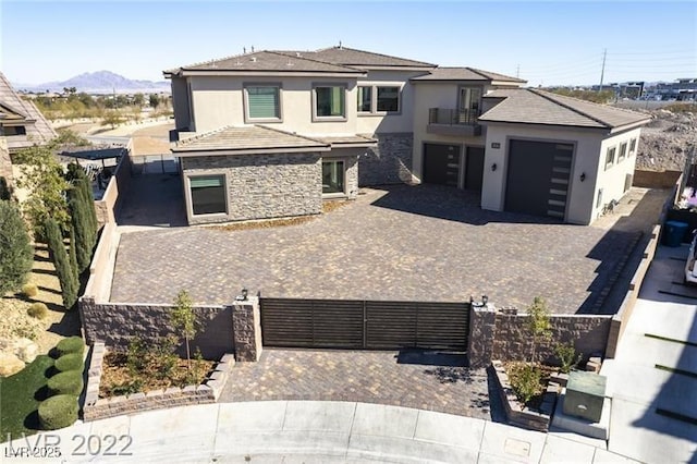 prairie-style house with stone siding, stucco siding, decorative driveway, and fence