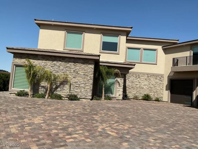 view of front of property with a balcony, decorative driveway, stucco siding, and stone siding