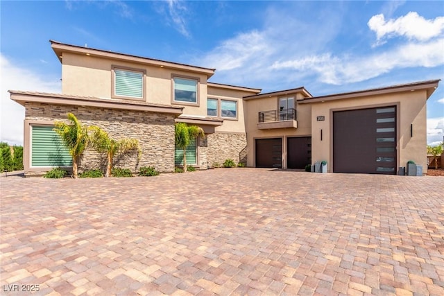 prairie-style house with stone siding, a balcony, decorative driveway, and stucco siding
