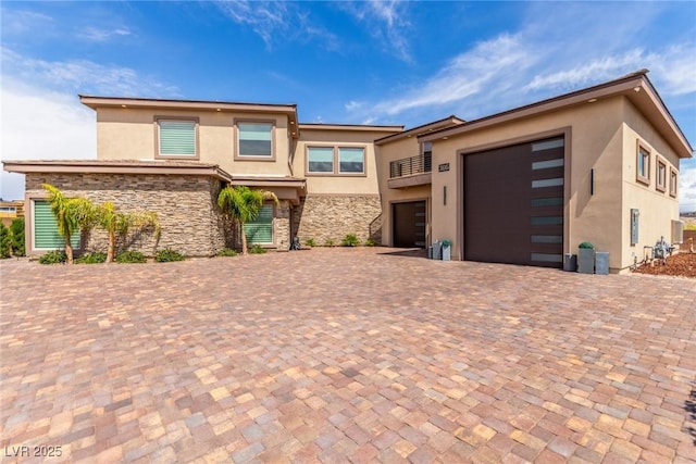 prairie-style house featuring stucco siding, a garage, stone siding, and decorative driveway