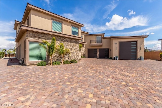 view of front of house featuring stone siding, a balcony, decorative driveway, and stucco siding