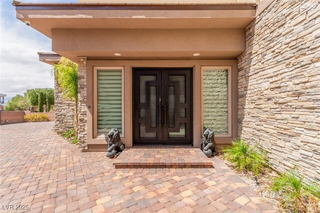 doorway to property featuring stucco siding, stone siding, and french doors