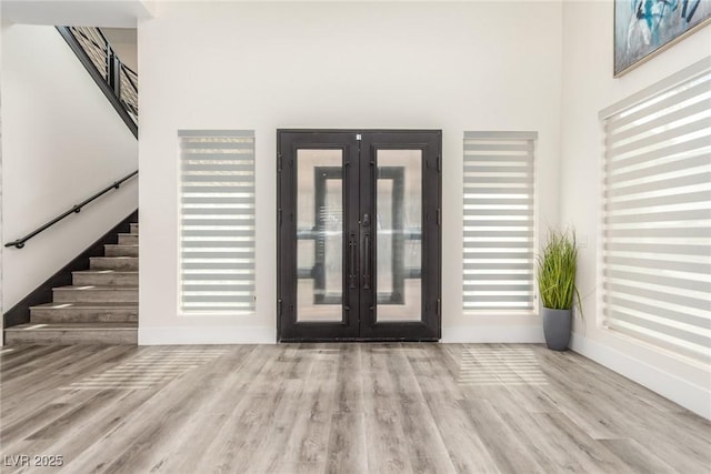 foyer entrance featuring french doors, a towering ceiling, stairway, and wood finished floors