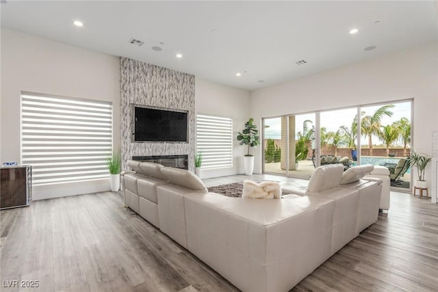 living area with a large fireplace, visible vents, recessed lighting, and wood finished floors