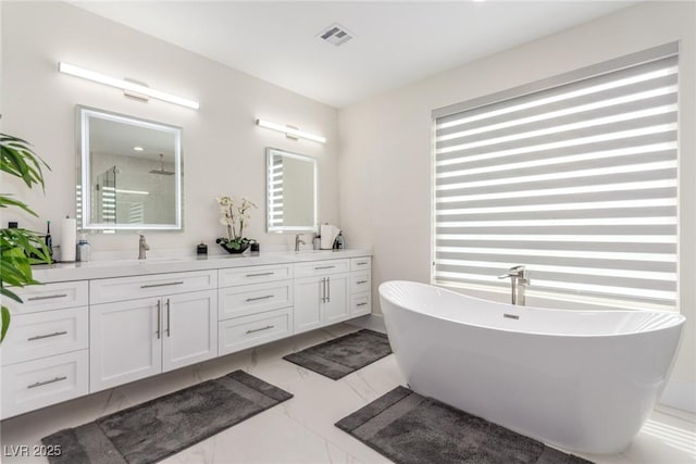 full bath with marble finish floor, a sink, visible vents, a freestanding bath, and double vanity