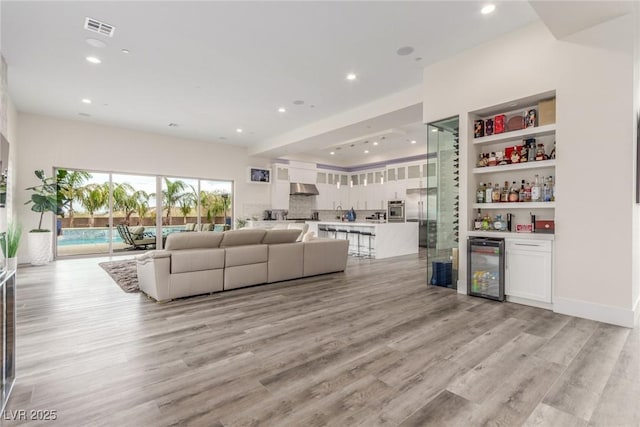 living area featuring beverage cooler, visible vents, light wood-style floors, a dry bar, and recessed lighting