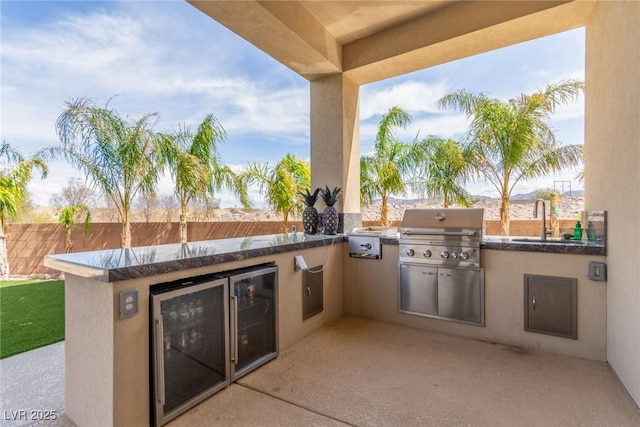 view of patio with fence, grilling area, a sink, beverage cooler, and an outdoor kitchen