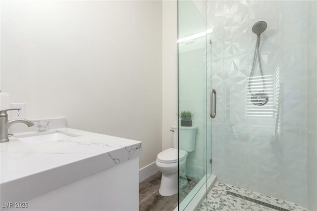 bathroom with a shower stall, baseboards, toilet, wood finished floors, and vanity