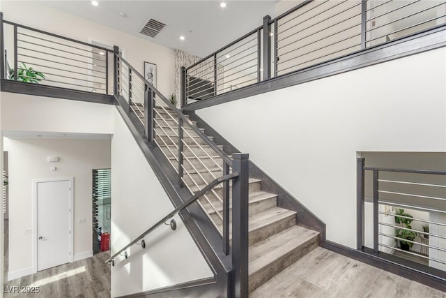 stairway with a high ceiling, visible vents, recessed lighting, and wood finished floors