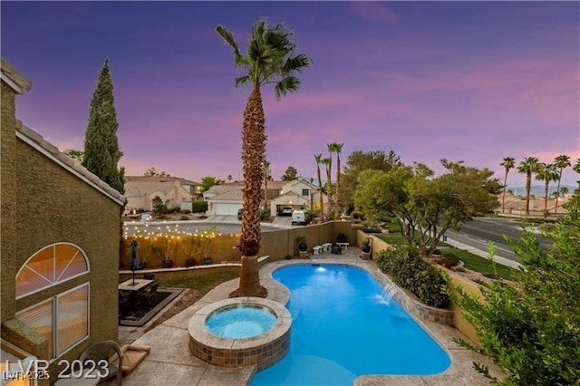 pool at dusk with a fenced backyard, a pool with connected hot tub, and a patio