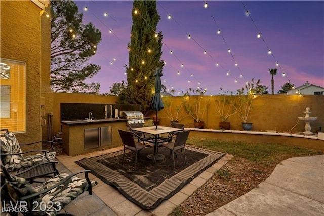 patio terrace at dusk with a sink, outdoor dining area, area for grilling, and fence