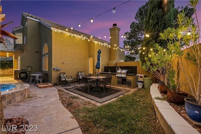 patio terrace at dusk featuring grilling area, exterior kitchen, and fence