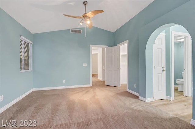 unfurnished bedroom with carpet, visible vents, baseboards, arched walkways, and vaulted ceiling