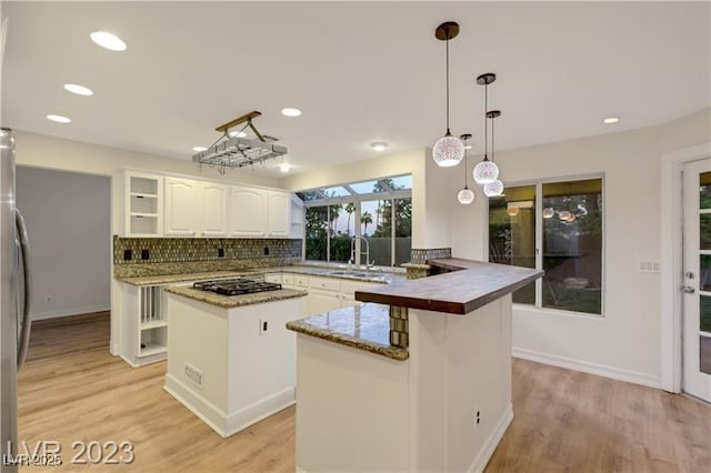 kitchen featuring a sink, gas cooktop, a kitchen island, tasteful backsplash, and a peninsula