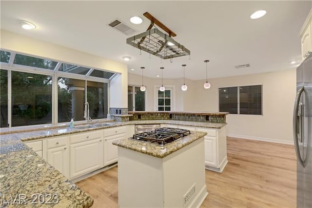 kitchen featuring visible vents, light wood-style flooring, a sink, a center island, and appliances with stainless steel finishes