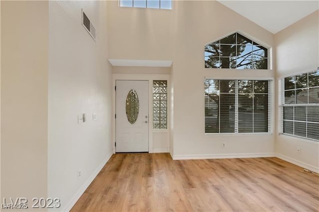 foyer entrance with visible vents, wood finished floors, baseboards, and a towering ceiling