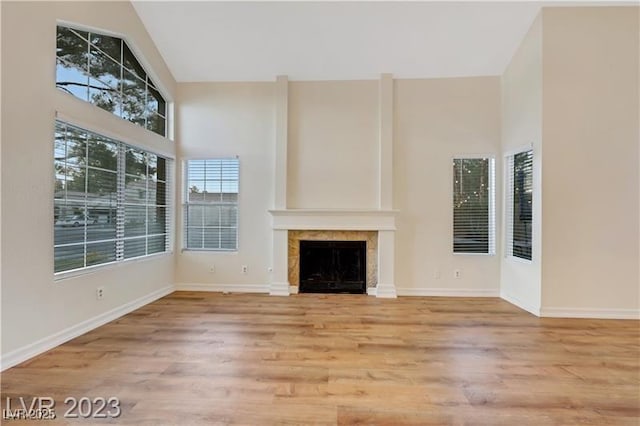 unfurnished living room with baseboards, high vaulted ceiling, wood finished floors, and a fireplace