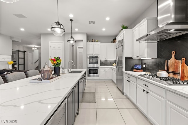 kitchen featuring visible vents, wall chimney range hood, a barn door, stainless steel appliances, and a sink