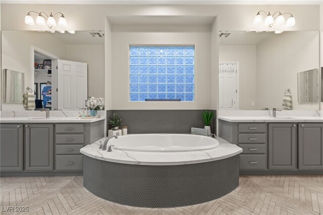 bathroom featuring a garden tub, two vanities, visible vents, and a sink