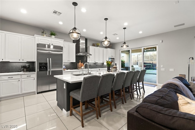 kitchen with light tile patterned floors, a sink, built in refrigerator, wall chimney range hood, and open floor plan