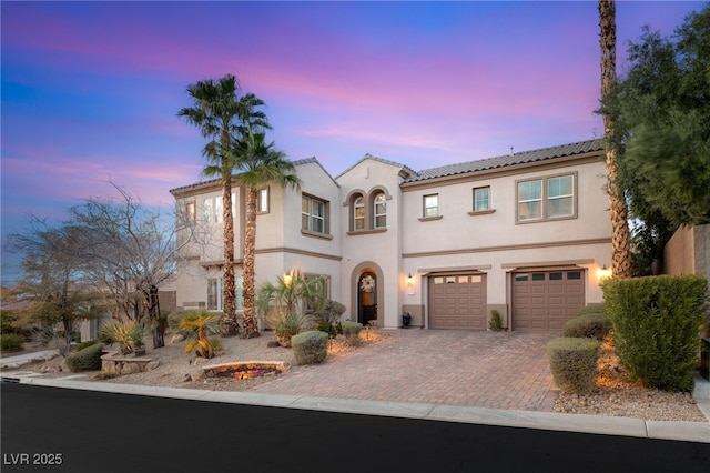 mediterranean / spanish home featuring stucco siding, decorative driveway, a garage, and a tiled roof