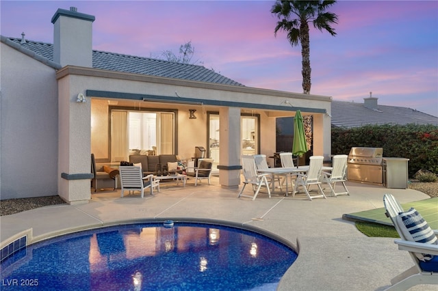 back of house at dusk with a patio area, a chimney, outdoor lounge area, and exterior kitchen