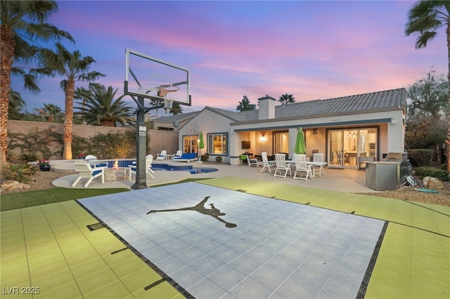 back of property at dusk featuring stucco siding, a patio, and a fenced in pool