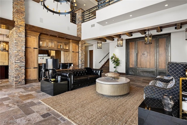 living room featuring visible vents, stairway, beamed ceiling, decorative columns, and stone tile floors