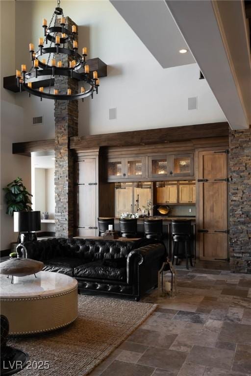 bar with stone finish flooring, a notable chandelier, visible vents, and a towering ceiling