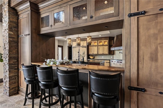 kitchen with premium range hood, glass insert cabinets, dark countertops, a breakfast bar area, and decorative backsplash