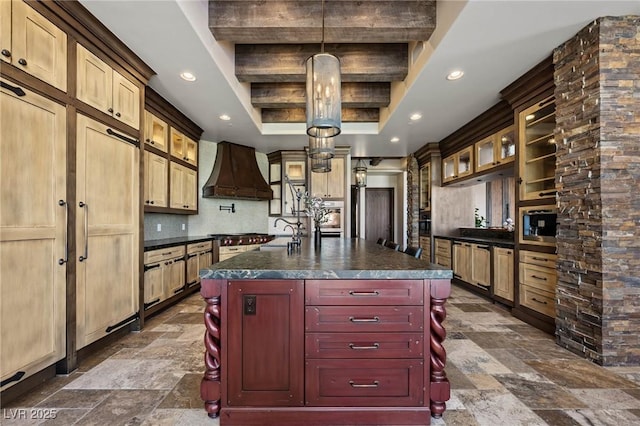 kitchen featuring dark countertops, backsplash, a center island with sink, custom exhaust hood, and stone finish floor