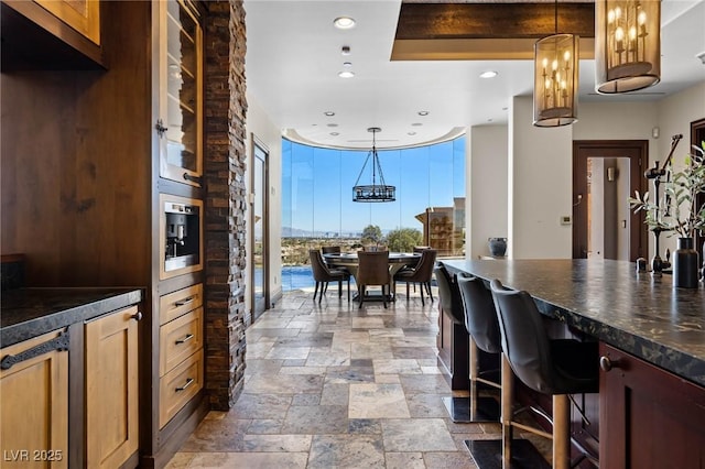 kitchen with recessed lighting, stone tile flooring, hanging light fixtures, glass insert cabinets, and dark countertops