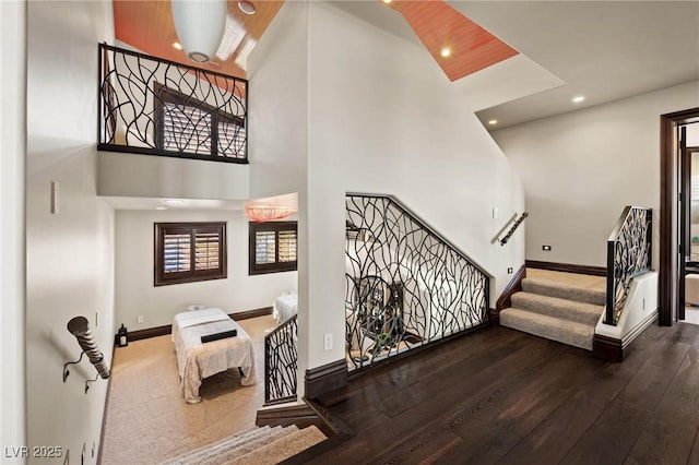 stairway featuring recessed lighting, baseboards, wood-type flooring, and a towering ceiling