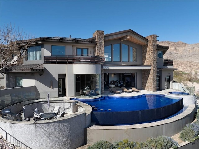 64 Promontory Ridge Dr, Las Vegas, NV 89135 - rear view of house with a balcony, an in-ground hot tub, stucco siding, and an outdoor pool