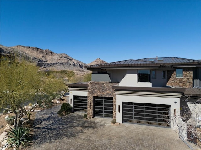 view of front of house featuring stucco siding, decorative driveway, a garage, stone siding, and a mountain view