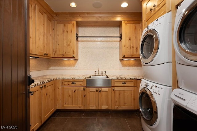 laundry room with a sink, recessed lighting, cabinet space, stacked washer / drying machine, and dark tile patterned flooring