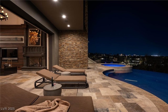 patio at night with an in ground hot tub and an outdoor fireplace