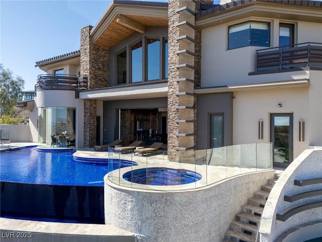 back of house featuring stucco siding, stone siding, a balcony, and a patio area