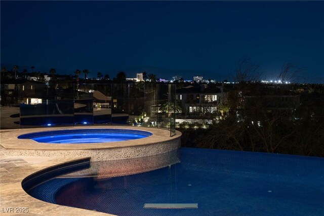 pool at night featuring an in ground hot tub