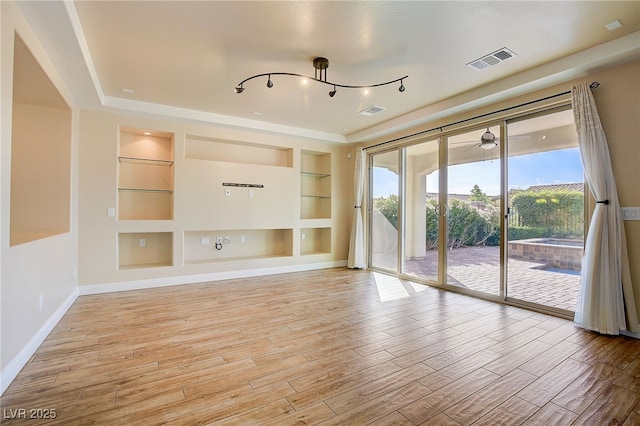 unfurnished living room with visible vents, built in shelves, baseboards, and wood finished floors