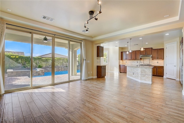 unfurnished living room featuring visible vents, track lighting, light wood-style floors, baseboards, and ceiling fan