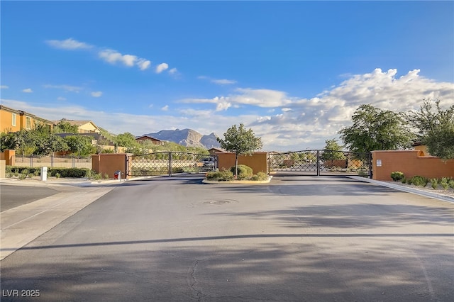 view of road with curbs, a mountain view, a gated entry, and a gate