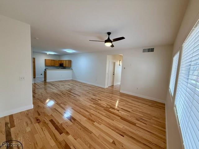 unfurnished living room featuring visible vents, baseboards, light wood-style floors, and a ceiling fan