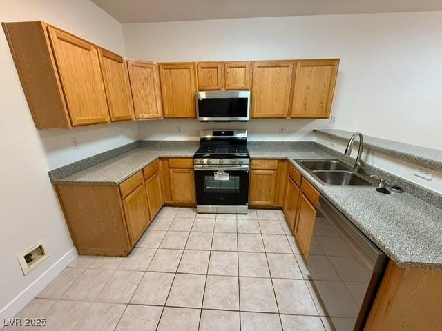 kitchen featuring baseboards, light tile patterned floors, brown cabinets, appliances with stainless steel finishes, and a sink